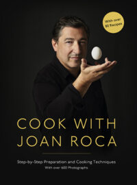 Joan Roca holding an egg wearing a black shirt with a black background